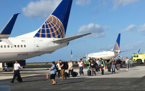 Passengers and crew leave a grounded United Airlines plane (right) after sleeping on the plane to board a "rescue" flight on 19 March