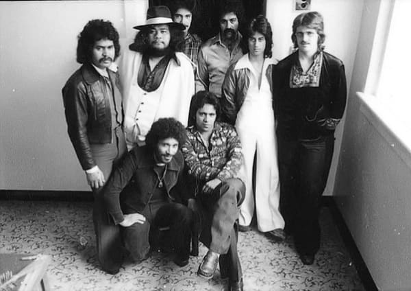 A group of '70s looking men stand in a cluster.