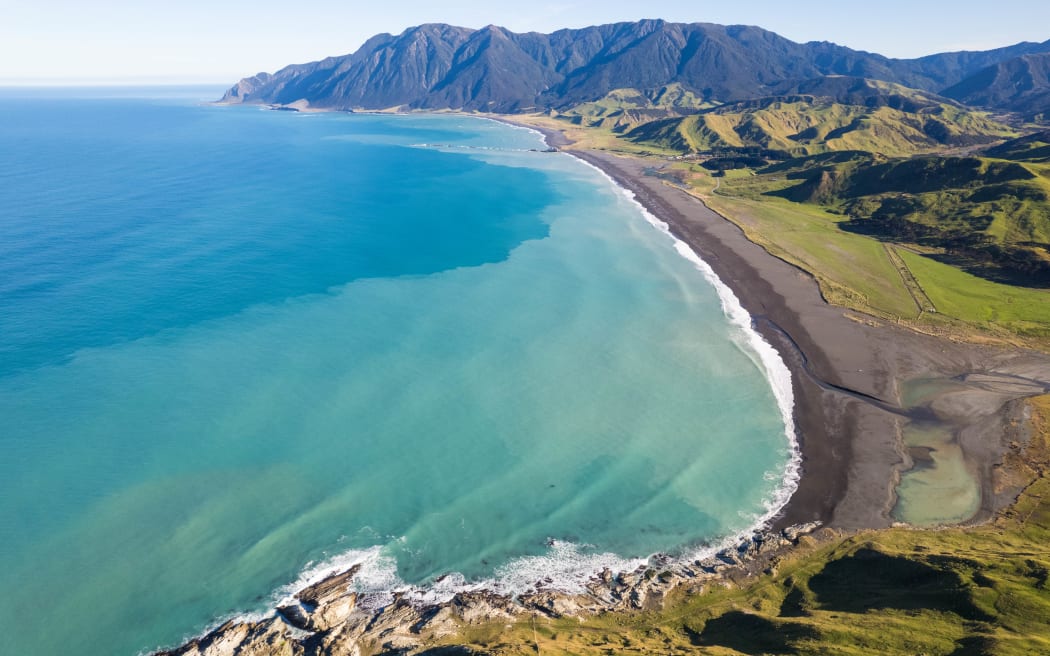 A drone shot above coastal water showing clear blue water on one side and brown, sediment-laden water to the right