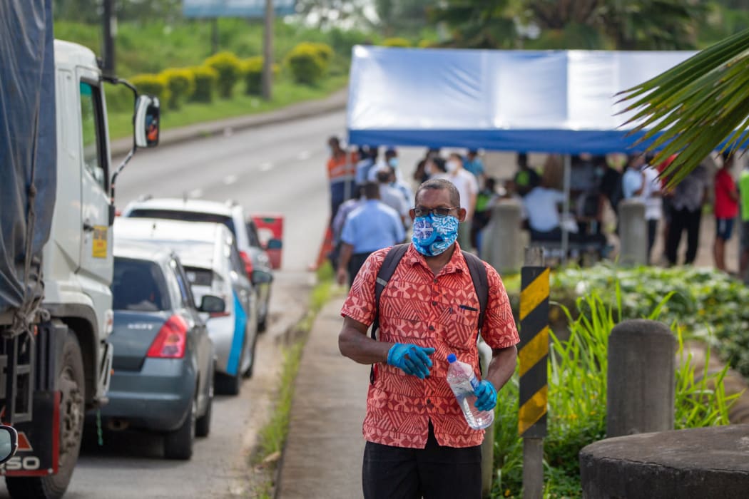 Person walks along the road as security officers check cars in Suva, Fiji on 26 April, 2021.