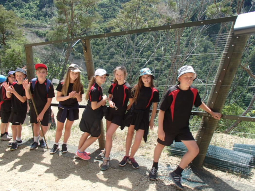School pupils walking up next to fence.