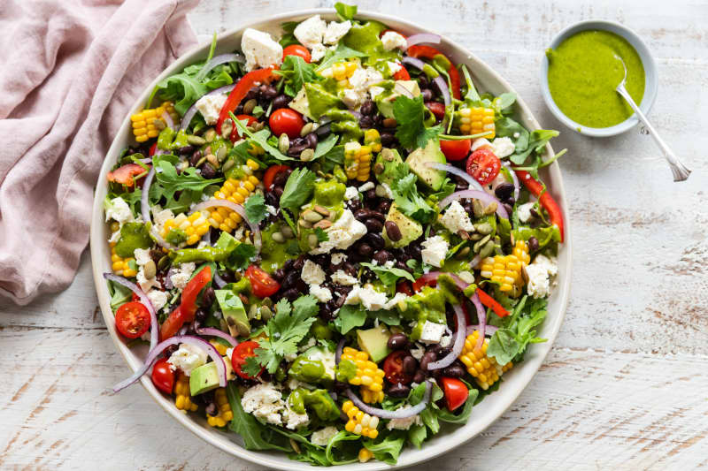 A round platter of containing Mexican black bean and corn salad with coriander dressing, with a small bowl of green dressing to the side.