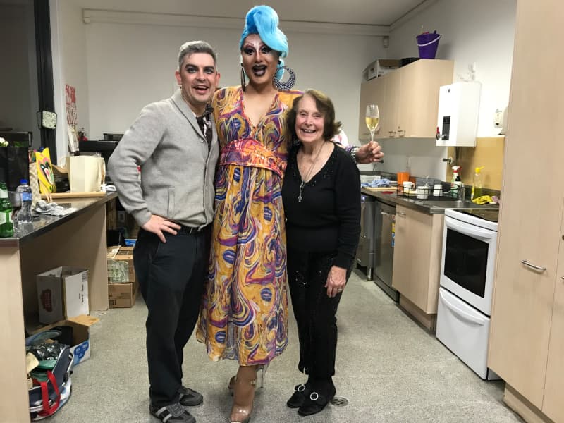 Three people stand together in a ktichen smiling for the camera.