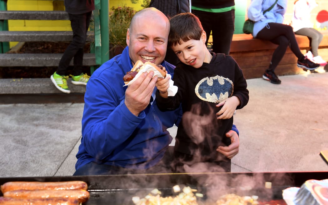 Australia's Treasurer Josh Frydenberg (L) enjoys a sausage with son Blake after voting during Australia's federal election in Melbourne on May 21, 2022. (Photo by William WEST / AFP)