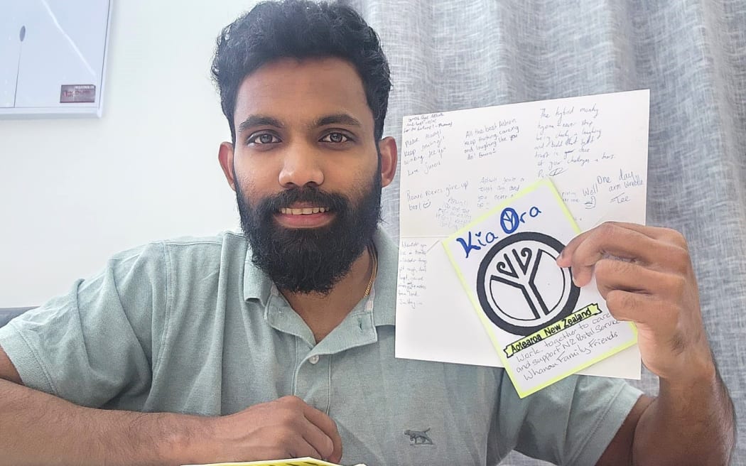 Photo of a man holding up a few letters and postcards, with more letters spread out on the table in front of him.