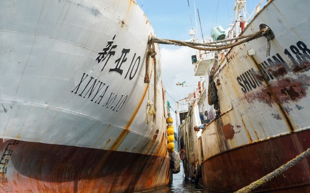 A child looks down at the water between two fishing boat hulks anchored in Suva harbor. 14 February 2025.