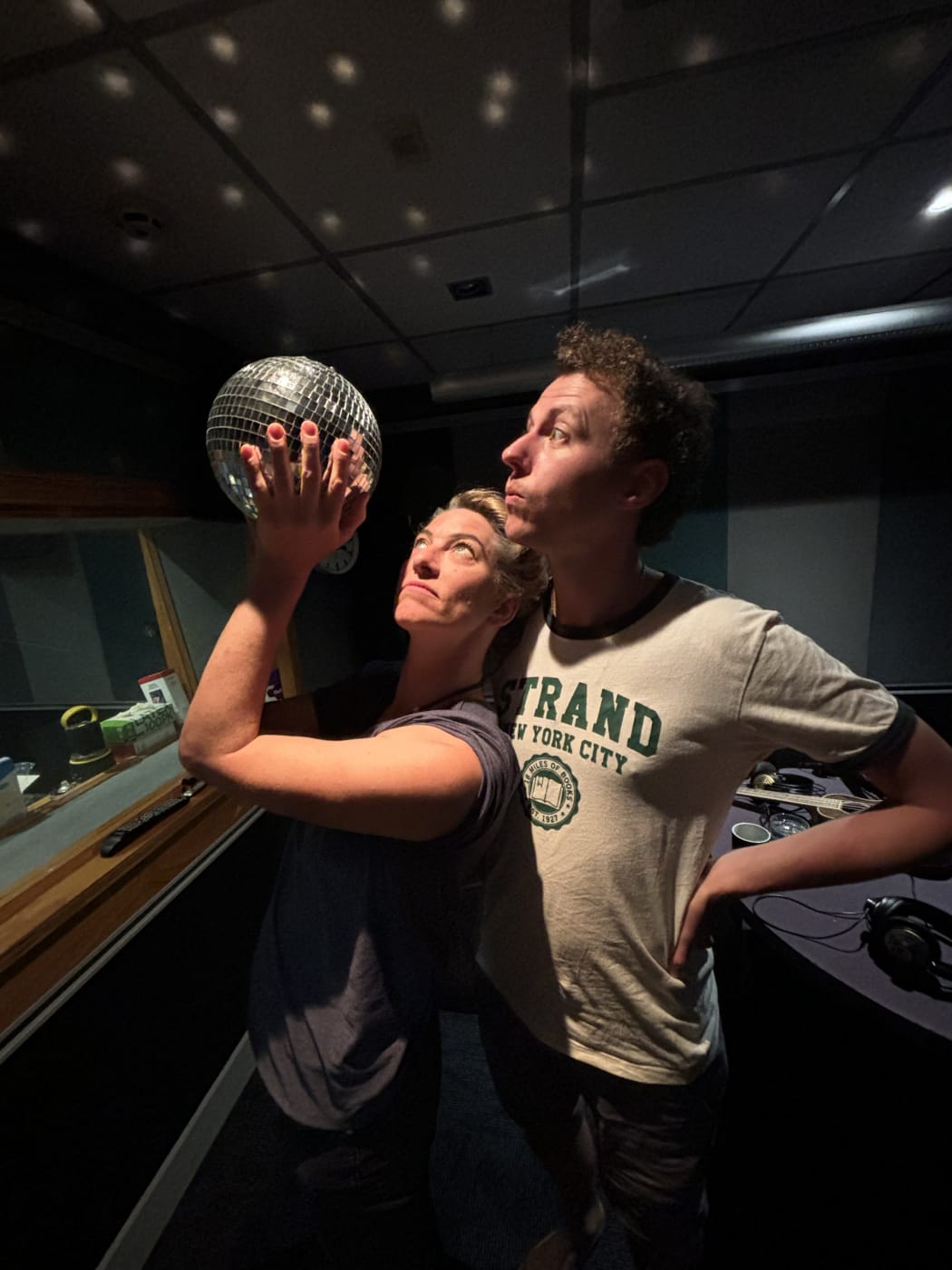 Amanda and Emile look reverently at a held disco ball, which casts light around the RNZ studio they're standing in.