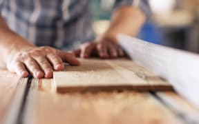 Closeup of a skilled carpenter sawing a piece of wood with a table saw while working alone in his woodworking studio