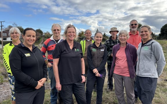A group of ten people smiling at the camera beneath a cloudy sky. They are all wearing clothes suitable for outdoor activity.