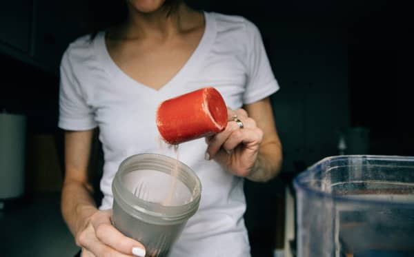 Woman pours scoop of powder into a mixer.
