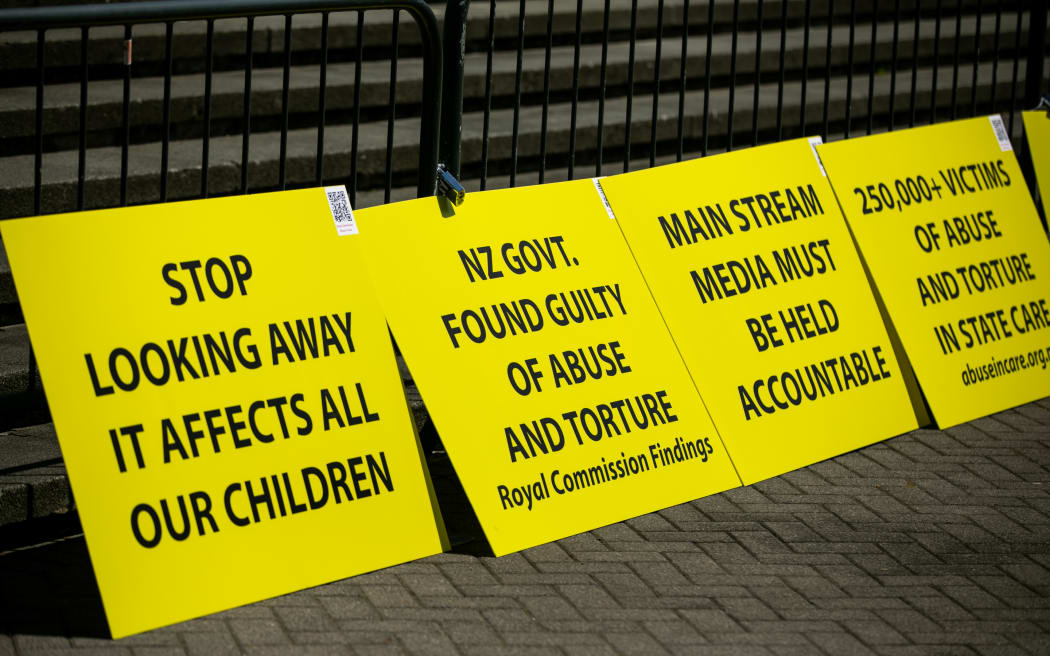 Signs from protestors sit outside Parliament during the apology for abuse in state care