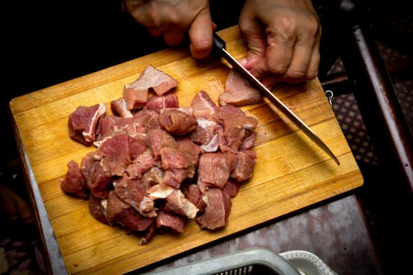 A person chops raw meat on a wooden chopping board.