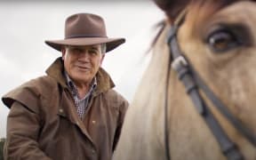 A still from a New Zealand First ad. Winston Peters is on a horse, wearing a cowboy hat. He grins at the camera.