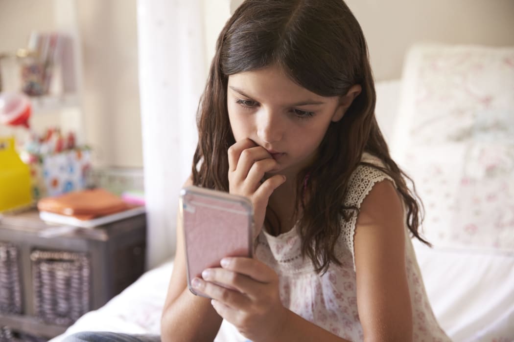 A photo of a young Girl In Bedroom Worried by what she's looking at on her phone