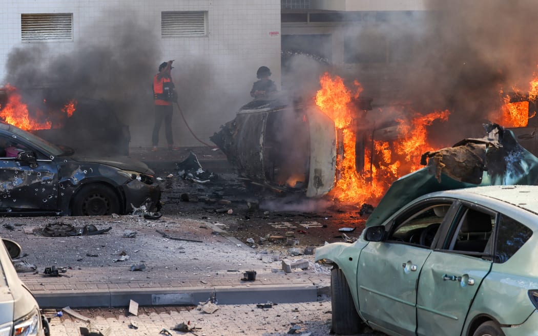 People try to extinguish fire on cars following a rocket attack from the Gaza Strip in Ashkelon, southern Israel, on October 7, 2023. Palestinian militant group Hamas has launched a "war" against Israel, Defence Minister Yoav Gallant said, after barrages of rockets were fired from the Gaza Strip into Israeli territory on October 7. (Photo by AHMAD GHARABLI / AFP)