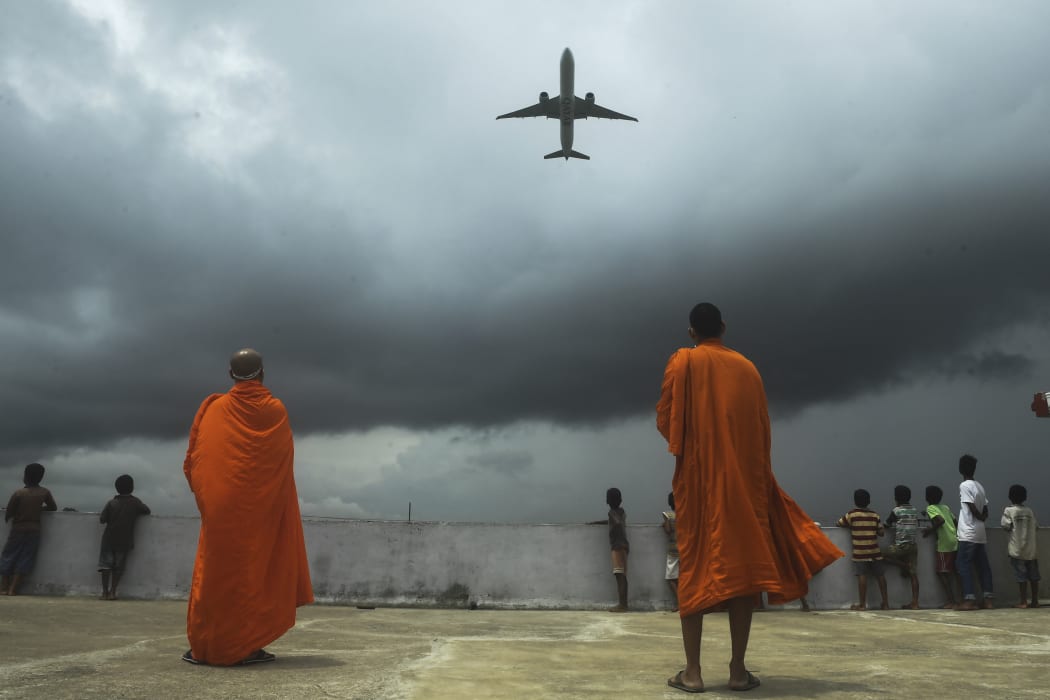 Buddhists monks and children look out from the rooftop at a Buddhist mission hostel and school for underprivileged children as an international passenger flight takes off from Kolkata, India.