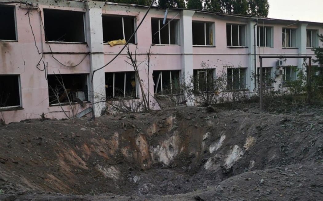 A large hole in the ground in front of a damaged building.