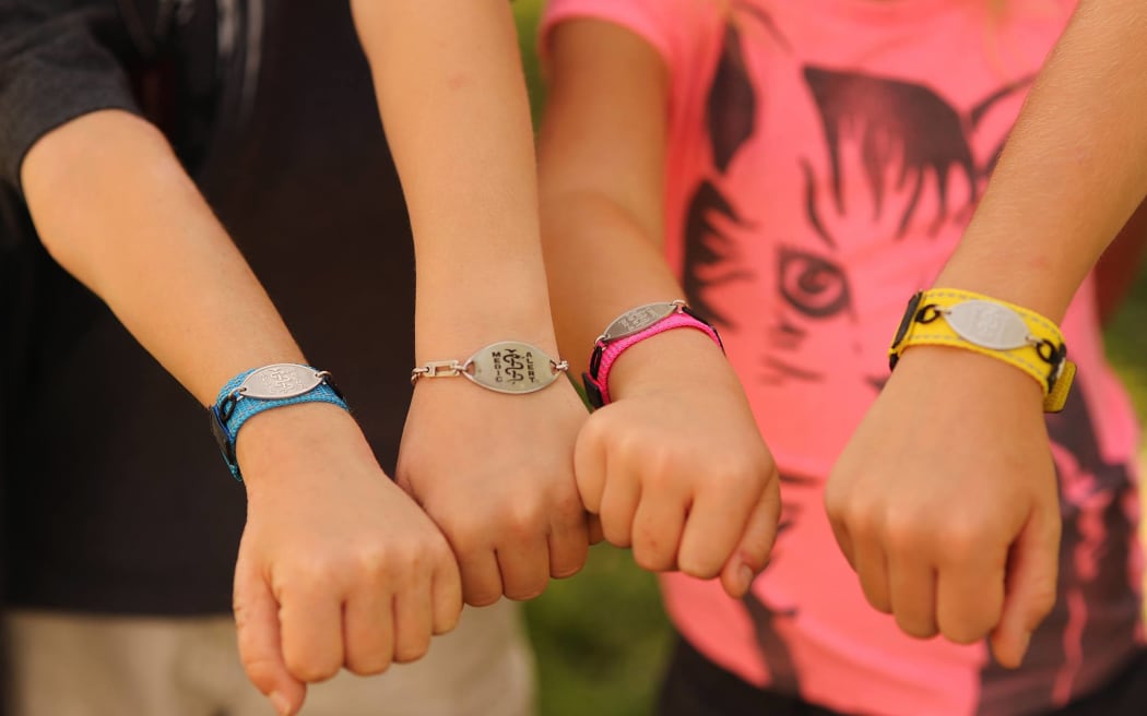 Children hold out arms wearing medic alert bracelets