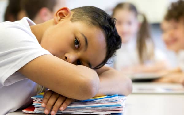 A close up shot of a little boy at school who looks distant and upset.