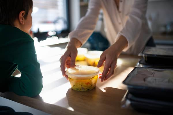 Woman opening a plastic container with soup for a child.