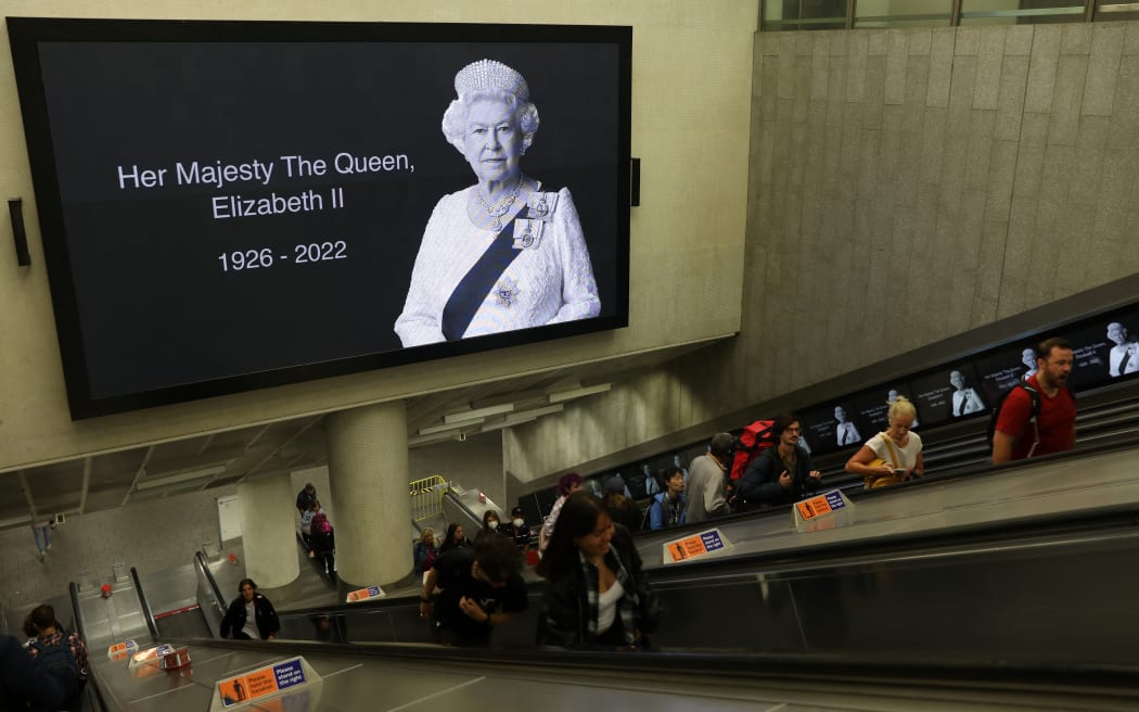 Commuters pass beneath a tribute image of Queen Elizabeth II as they travel through Kings Cross train station in London on September 10, 2022, two days after The Queen died at the age of 96. - King Charles III pledged to follow his mother's example of "lifelong service" in his inaugural address to Britain and the Commonwealth on Friday, after ascending to the throne following the death of Queen Elizabeth II on September 8. (Photo by ISABEL INFANTES / AFP)