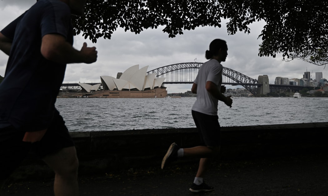 People run before the Opera House and Harbour Bridge in Sydney on December 20, 2020, after authorities introduced a fresh round of restrictions.