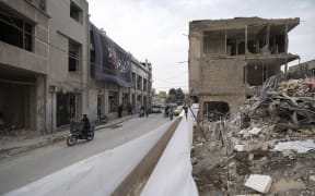 An Iranian motorcyclist rides past a building that was destroyed during a military operation near a police station in a residential area in Tehran, Iran, on March 15, 2026. (Photo by Morteza Nikoubazl/NurPhoto) (Photo by Morteza Nikoubazl / NurPhoto via AFP)