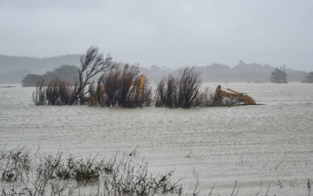 Heavy machinery caught in floodwater at the Wairoa River mouth. The digger is used to open up a channel in the bar to let floodwater escape more quickly.