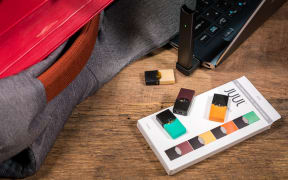 A JUUL device charges on a laptop, beside JUUL pods.