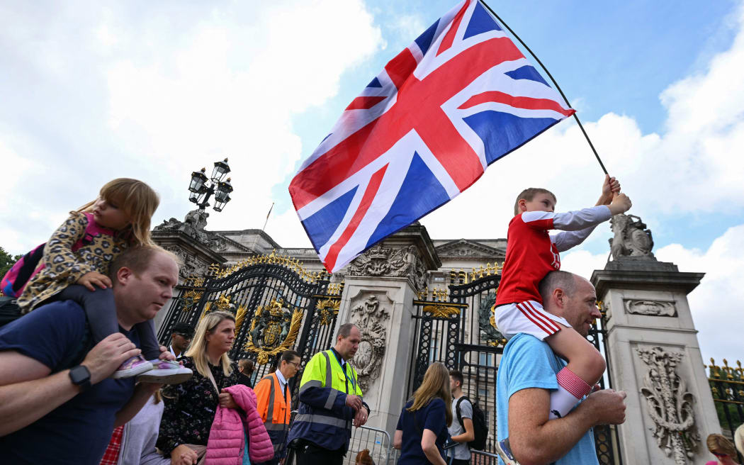 A boy waves a Britain national flag as others gather outside of Buckingham Palace in London on September 11, 2022. - Queen Elizabeth II's coffin will travel by road through Scottish towns and villages on Sunday as it begins its final journey from her beloved Scottish retreat of Balmoral. The Queen, who died on September 8, will be taken to the Palace of Holyroodhouse before lying at rest in St Giles' Cathedral, before travelling onwards to London for her funeral. (Photo by SEBASTIEN BOZON / AFP)