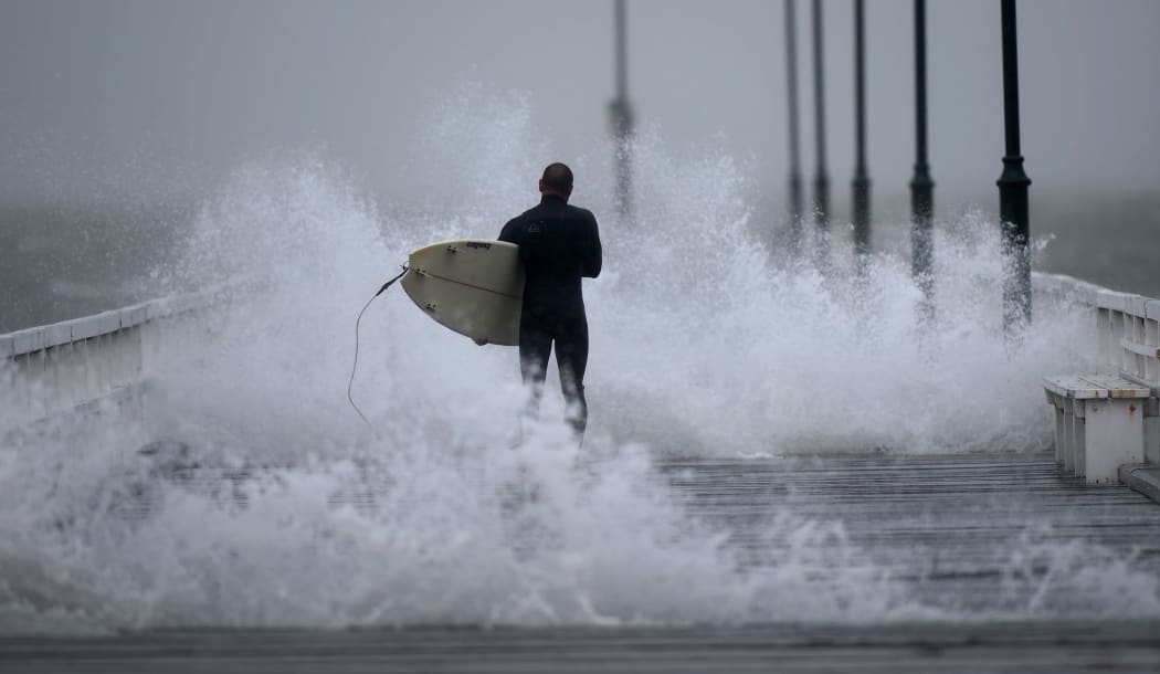 A surfer makes his way along the pier before jumping off into Port Phillip Bay as the storm lashes the Melbourne area.