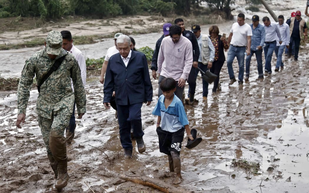 Mexican President Andres Manuel Lopez Obrador (third from left) and members of his cabinet walk on the mud as they visit the El Kilometro 42 community, near Acapulco, Guerrero State, Mexico, after the passage of Hurricane Otis, on 25 October, 2023.