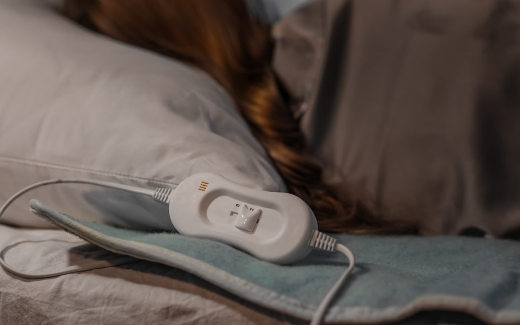Young woman sleeping on electric heating pad in bedroom at night.