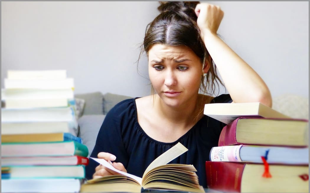 Image of student looking confused surrounded by books.