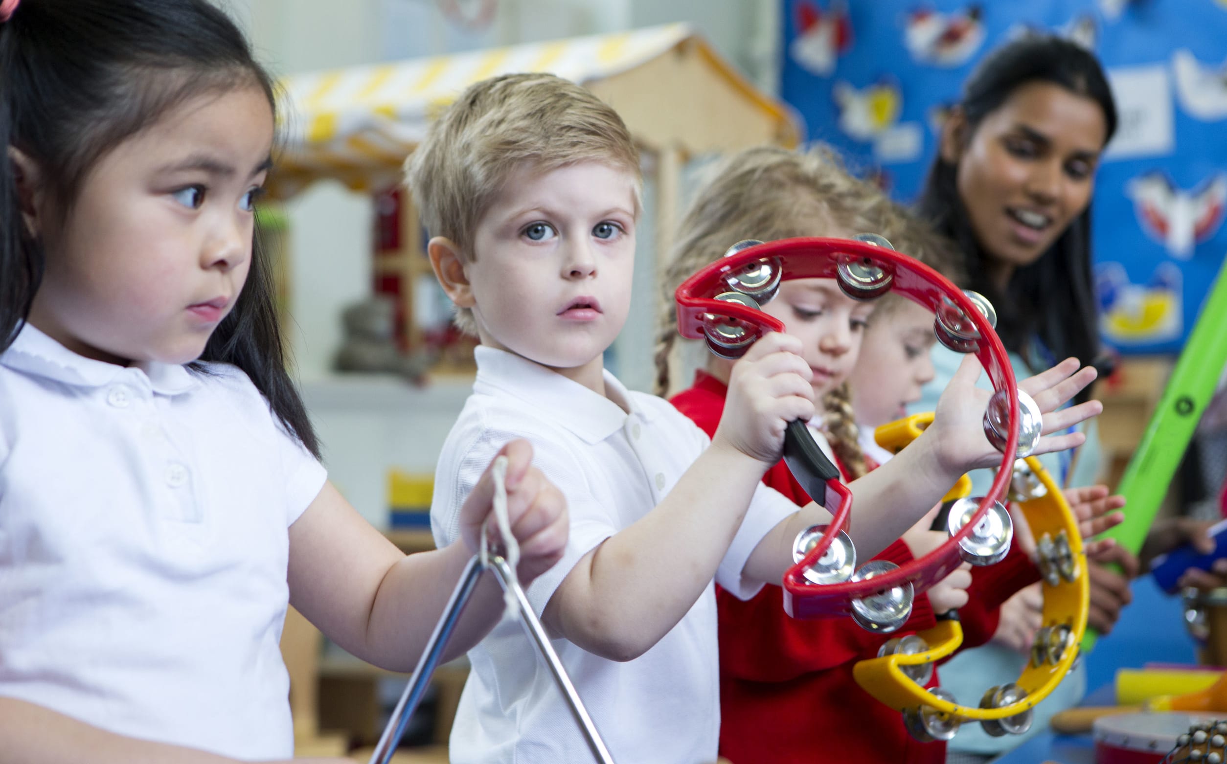 A photo of a young children playing musical instruments. The girl in the foreground looks worried but is joining in.