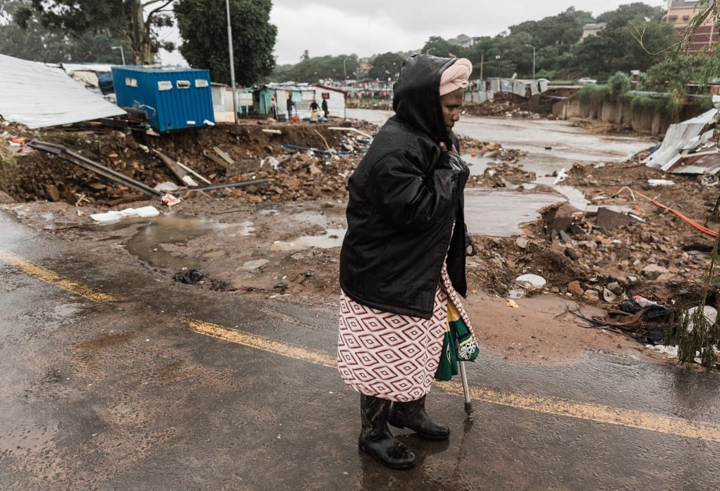 A woman in a drenched raincoat walks pass the Quarry road informal settlement outside Durban on April 18, 2022 as rain begins to fall once again after winds, heavy rainfall and mudslides destroyed many homes and infrastructure last week.