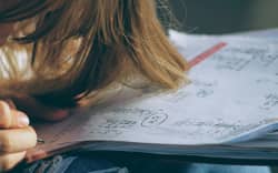 A teenager working on maths problems on a worksheet.