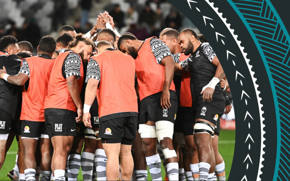 A photo of the Fiji team. Their backs are to the camera and the they are in a circle, with hands clasped and heads bowed in prayer prior to a match.