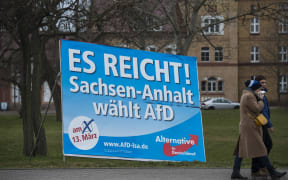 A couple walks past a campaign poster for right-wing populist Alternative for Germany party reading: "Enough is enough, Saxony-Anhalt votes for AfD", in Magdeburg, eastern Germany.