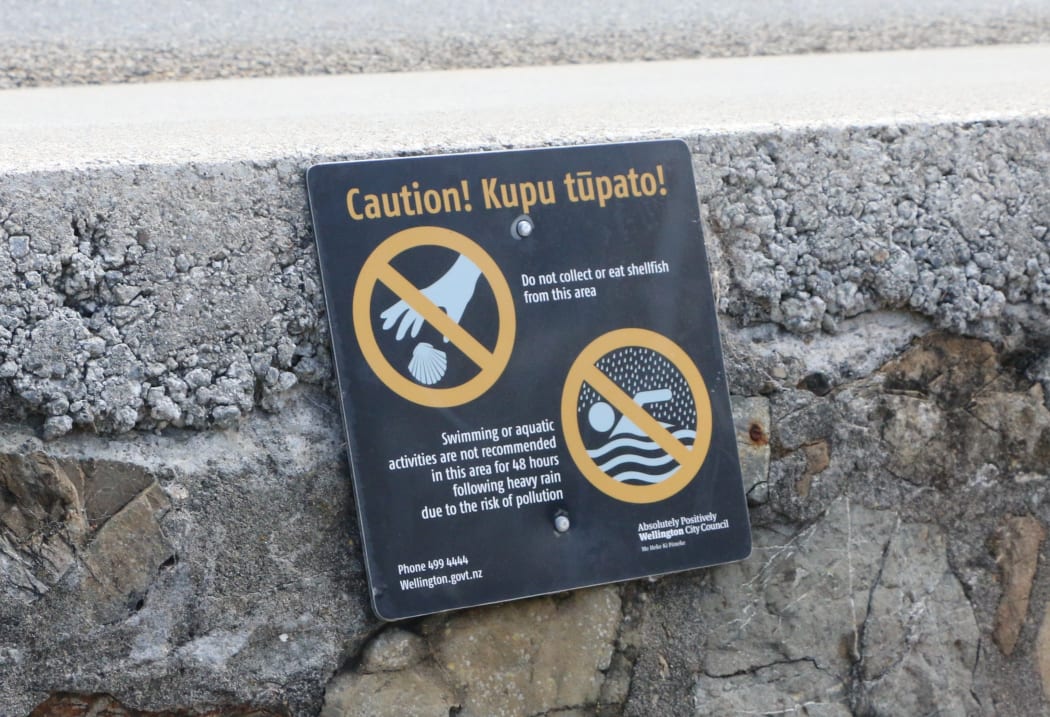A sign at Ōwhiro Bay warns people not to take shellfish or swim after rain. Karori residents want similar signs to warn people to stay out of the polluted stream, but Wellington Water has refused to erect any.