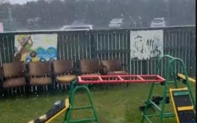 The play set is pictured on some grass in a fenced off area next to a carpark.