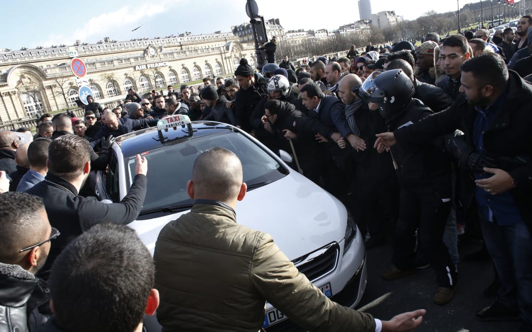 Non-licensed private hire cab drivers try to make way to allow a taxi to pass during a protest by non-licensed private hire cab drivers against the government's decision about their sector, in Paris on February 3, 2016, a week after angry French taxi drivers blocked key roads to protest against competition they judge unfair. The French Transportation ministry has sent formal notices last week to twenty of the transport network platforms (Uber, SnapCar, Driver-Private..) to remind them that the Loti (public transport on demand) licenses that regulate transportation, easier to get than the VTC (private hire cars) driving cards, apply only to collective transport, cars that carry at least two passengers.  AFP PHOTO / THOMAS SAMSON (Photo by THOMAS SAMSON / AFP)