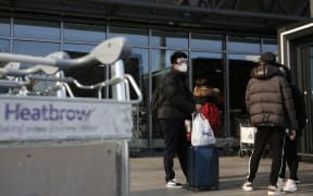 Travellers wearing a mask wait oustside an Heathrow's airport terminal, in west London, on March 16, 2020.