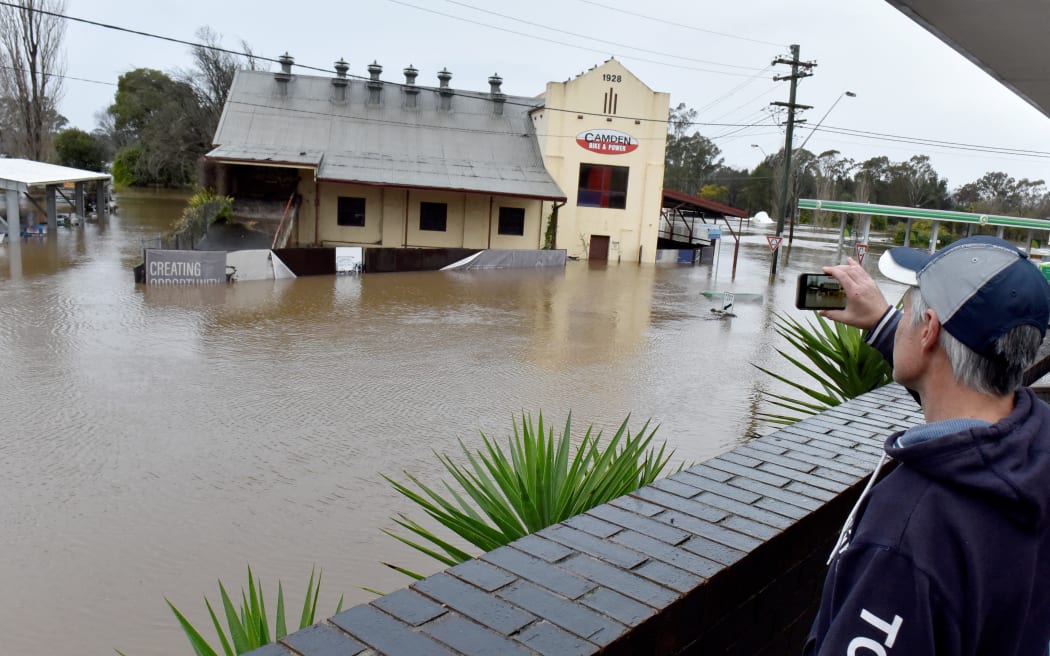 A man films flooded streets due to torrential rain in the Camden suburb of Sydney on July 3, 2022. - Thousands of Australians were ordered to evacuate their homes in Sydney on July 3 as torrential rain battered the country's largest city and floodwaters inundated its outskirts. (Photo by Muhammad FAROOQ / AFP)