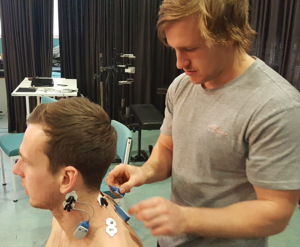 Jayden Pinfold attaches electrodes to volunteer Lorenz Kissling's neck.