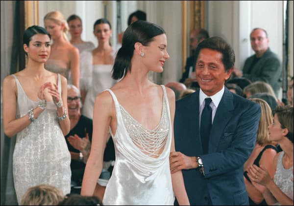 Italian designer Valentino holds the arm of a model 19 July in Paris at the end of his 1998/99 Fall/Winter haute couture collection. Black, white and gray dominated the show. (Photo by Thomas COEX / AFP)