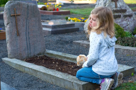 A photo of a little sad girl in front of grave