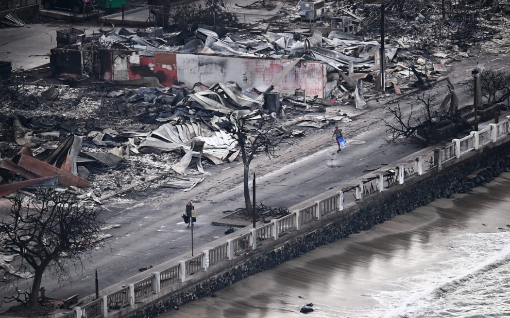 An aerial image taken on August 10, 2023 shows a person walking down Front Street past destroyed buildings burned to the ground in Lahaina in the aftermath of wildfires in western Maui, Hawaii. At least 36 people have died after a fast-moving wildfire turned Lahaina to ashes, officials said August 9, 2023 as visitors asked to leave the island of Maui found themselves stranded at the airport. The fires began burning early August 8, scorching thousands of acres and putting homes, businesses and 35,000 lives at risk on Maui, the Hawaii Emergency Management Agency said in a statement. (Photo by Patrick T. Fallon / AFP)