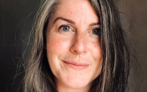 A slightly smiling woman with grey-streaked brown hair.