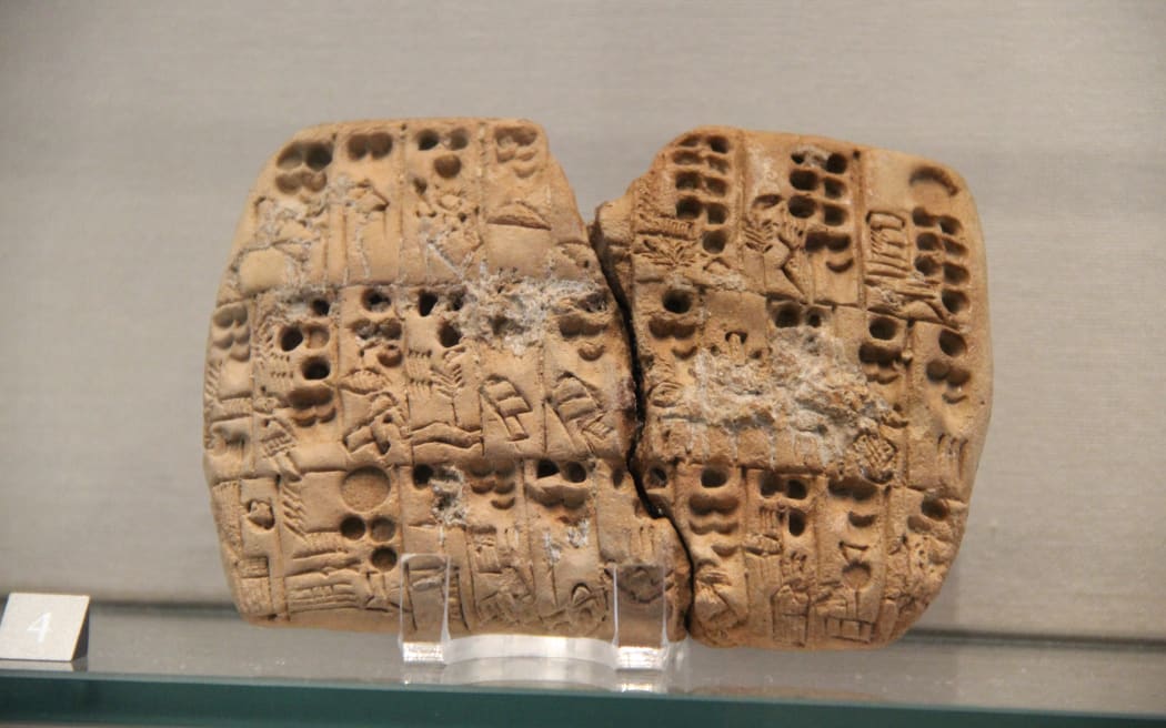 An ancient clay tablet which has split into two, displayed at a museum. The photo is close up to the artifact.